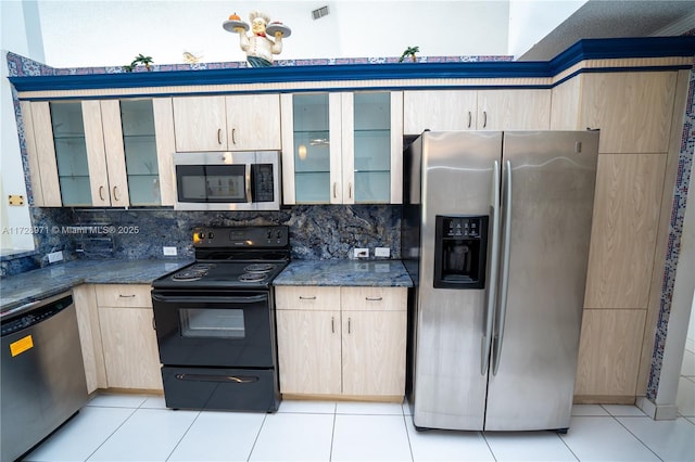 kitchen with light brown cabinetry, appliances with stainless steel finishes, tasteful backsplash, light tile patterned floors, and dark stone countertops