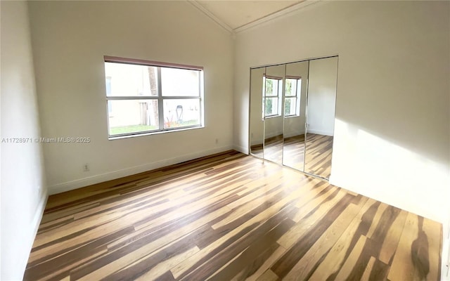 unfurnished bedroom with hardwood / wood-style flooring, a closet, high vaulted ceiling, and ornamental molding