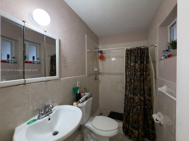 bathroom with a textured ceiling, sink, tile walls, toilet, and walk in shower