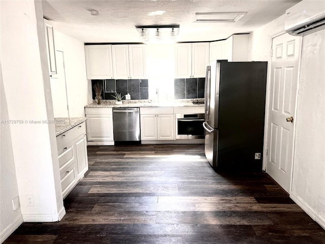 kitchen featuring dark wood-type flooring, appliances with stainless steel finishes, white cabinetry, a wall unit AC, and light stone countertops