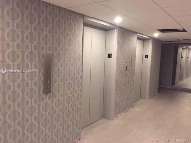 hall featuring elevator, a drop ceiling, and light hardwood / wood-style floors