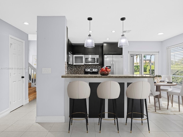 kitchen featuring kitchen peninsula, pendant lighting, tasteful backsplash, a kitchen bar, and stainless steel appliances