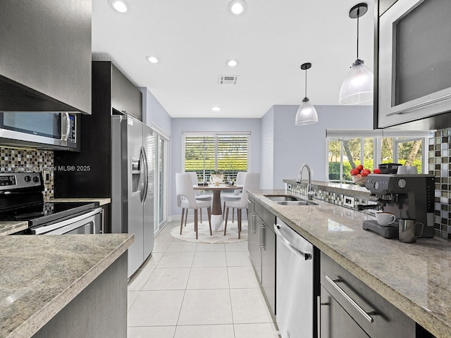 kitchen with appliances with stainless steel finishes, sink, decorative light fixtures, backsplash, and light tile patterned floors