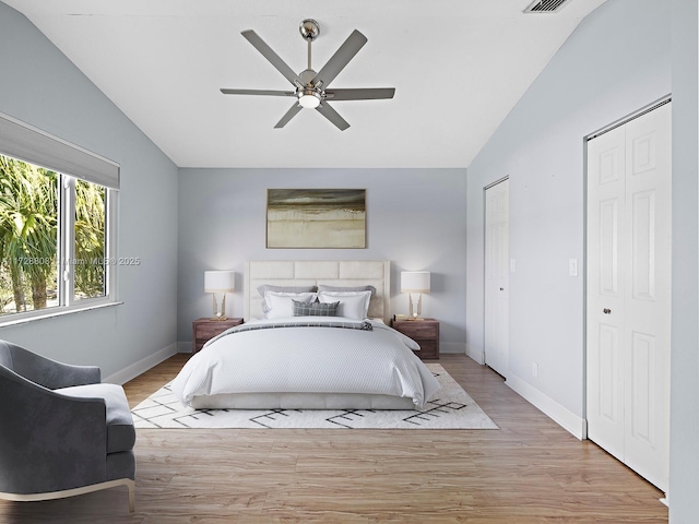 bedroom with ceiling fan, multiple closets, light hardwood / wood-style flooring, and vaulted ceiling