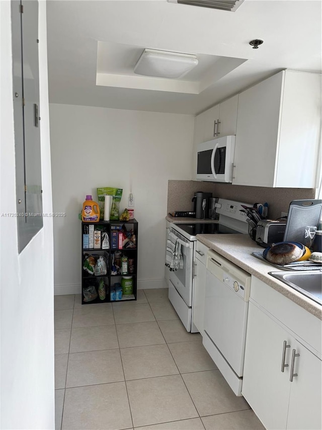 kitchen featuring light tile patterned flooring, sink, a raised ceiling, white appliances, and white cabinets