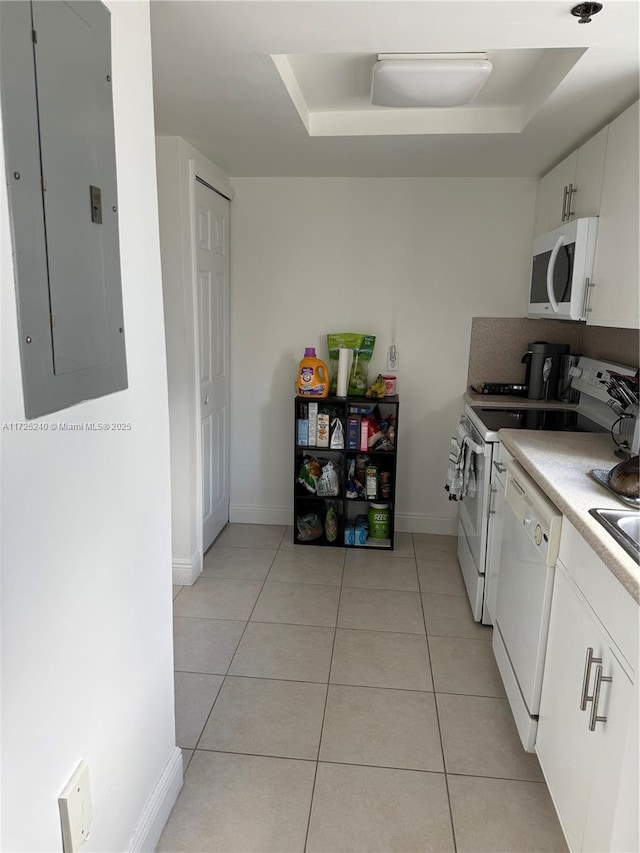 kitchen featuring light tile patterned flooring, white cabinets, electric panel, a tray ceiling, and white appliances