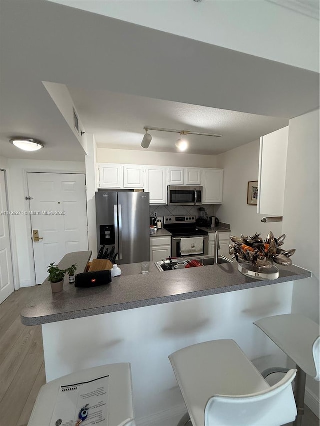 kitchen featuring kitchen peninsula, a kitchen bar, white cabinetry, and appliances with stainless steel finishes