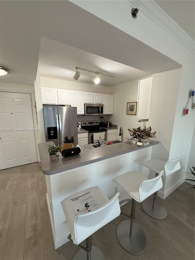 kitchen with kitchen peninsula, light wood-type flooring, white cabinetry, and appliances with stainless steel finishes