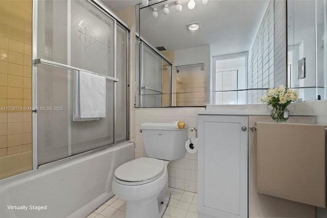 full bathroom featuring shower / bath combination with glass door, tile patterned flooring, vanity, tile walls, and toilet