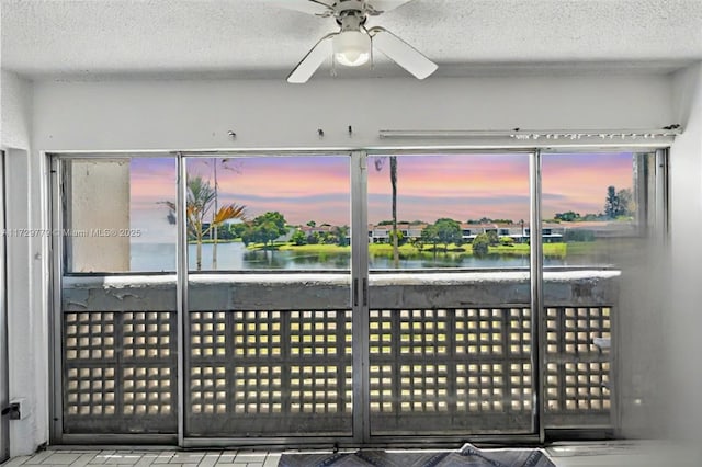 interior space with ceiling fan, a water view, and a textured ceiling