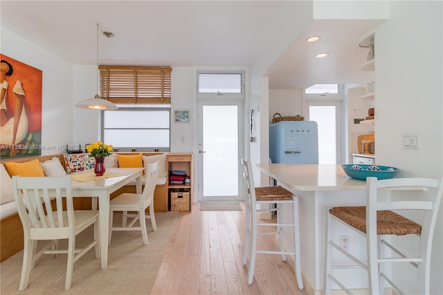 kitchen featuring decorative light fixtures, fridge, light hardwood / wood-style floors, and a kitchen breakfast bar