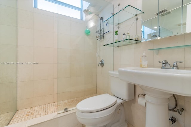 bathroom with tile walls, toilet, a tile shower, and tasteful backsplash