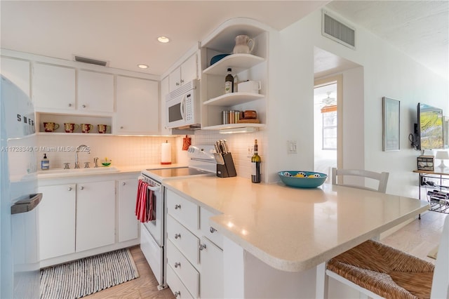 kitchen featuring kitchen peninsula, white appliances, a kitchen bar, and white cabinetry