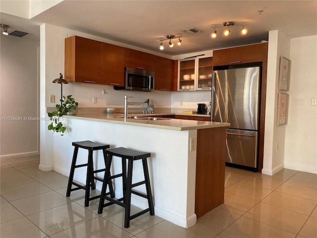 kitchen featuring a kitchen bar, appliances with stainless steel finishes, sink, kitchen peninsula, and light tile patterned flooring