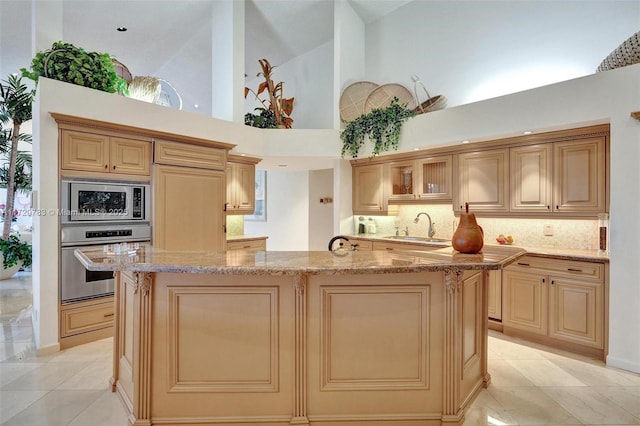 kitchen featuring stainless steel appliances, high vaulted ceiling, light stone counters, and a kitchen island with sink