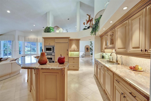 kitchen featuring light stone countertops, a kitchen island, light brown cabinets, stainless steel appliances, and backsplash