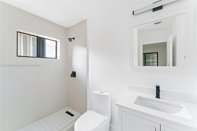 bathroom with vanity, tiled shower, and toilet