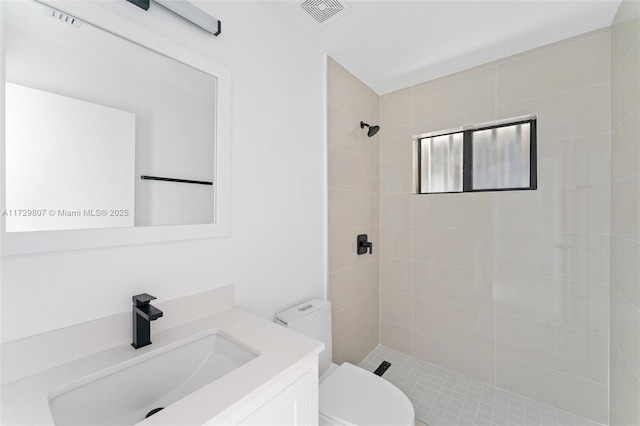 bathroom with vanity, tiled shower, and toilet