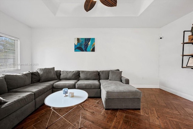 living room with a tray ceiling, dark parquet flooring, and ceiling fan