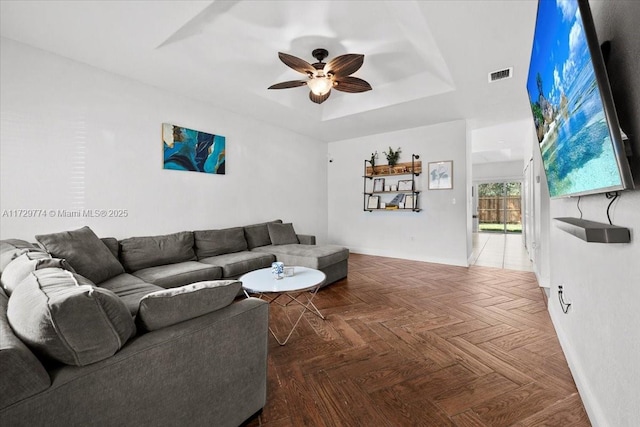 living room featuring ceiling fan, dark parquet flooring, and a raised ceiling