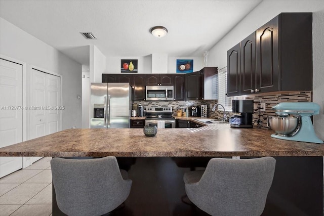 kitchen featuring appliances with stainless steel finishes, sink, tasteful backsplash, light tile patterned floors, and a kitchen bar