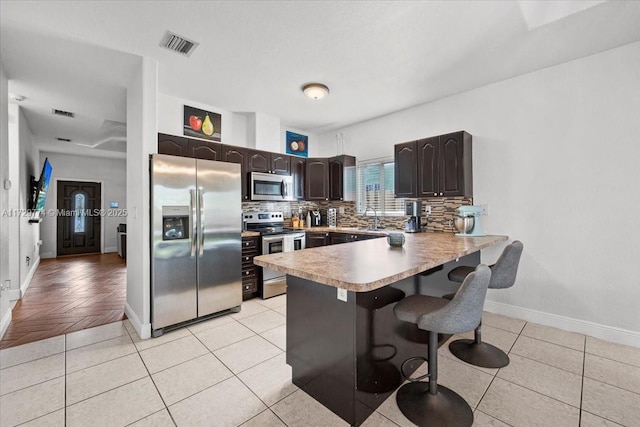 kitchen featuring a breakfast bar, appliances with stainless steel finishes, kitchen peninsula, and light tile patterned flooring