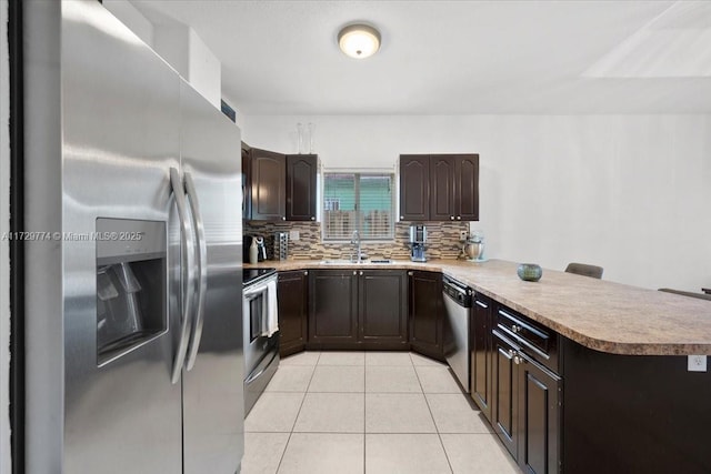 kitchen featuring appliances with stainless steel finishes, tasteful backsplash, light tile patterned floors, kitchen peninsula, and a breakfast bar