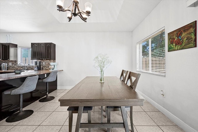 dining space with an inviting chandelier, light tile patterned floors, and a tray ceiling