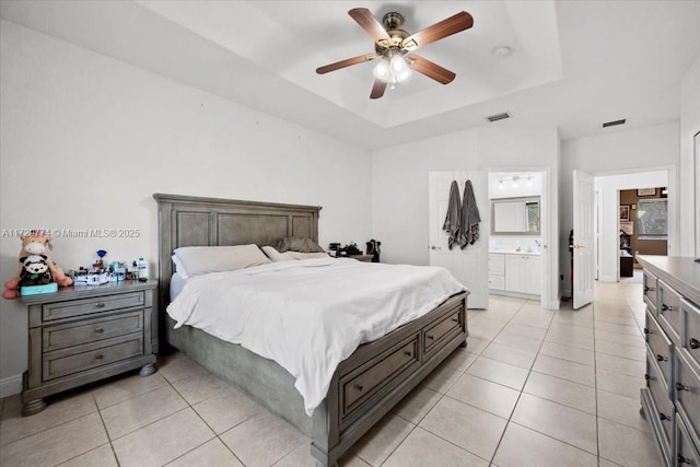 bedroom with ceiling fan, connected bathroom, a tray ceiling, and light tile patterned flooring