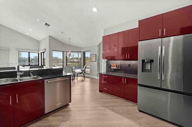 kitchen with lofted ceiling, stainless steel appliances, sink, a chandelier, and light wood-type flooring