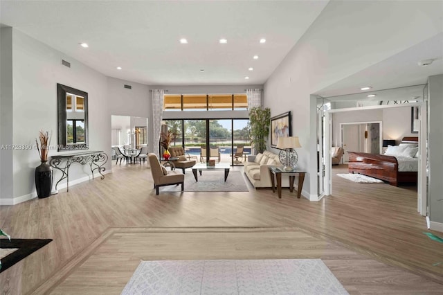 living room featuring a healthy amount of sunlight, light hardwood / wood-style flooring, and a towering ceiling