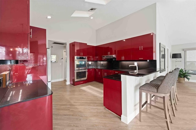 kitchen featuring fridge, double oven, high vaulted ceiling, kitchen peninsula, and a breakfast bar area