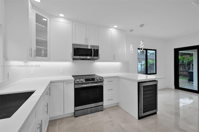 kitchen with appliances with stainless steel finishes, beverage cooler, white cabinets, decorative light fixtures, and kitchen peninsula