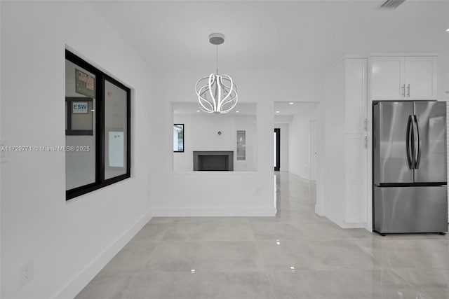 interior space with white cabinetry, pendant lighting, stainless steel fridge, and a chandelier