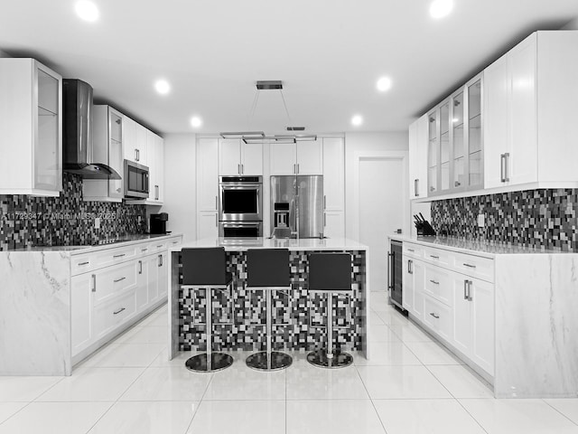 kitchen featuring light stone countertops, stainless steel appliances, white cabinetry, and wall chimney exhaust hood