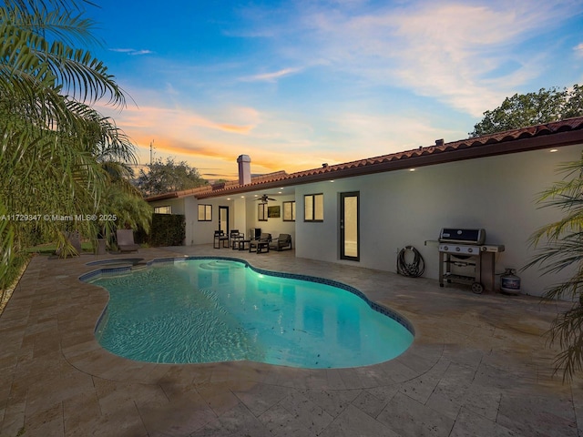 pool at dusk featuring a patio area, grilling area, and ceiling fan