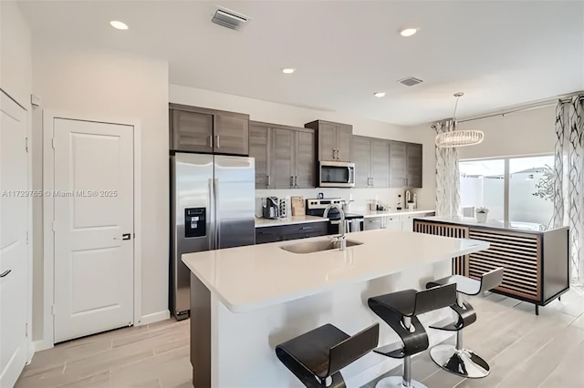 kitchen featuring appliances with stainless steel finishes, decorative light fixtures, an island with sink, sink, and a breakfast bar area