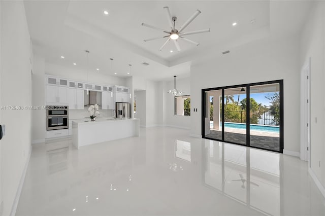 unfurnished living room featuring ceiling fan with notable chandelier and a raised ceiling