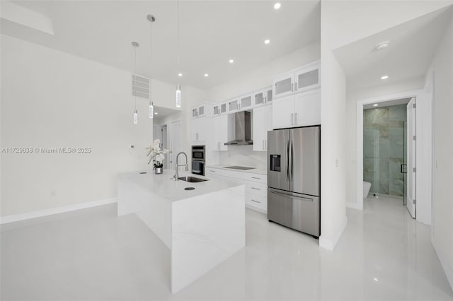 kitchen with appliances with stainless steel finishes, white cabinetry, hanging light fixtures, an island with sink, and wall chimney exhaust hood