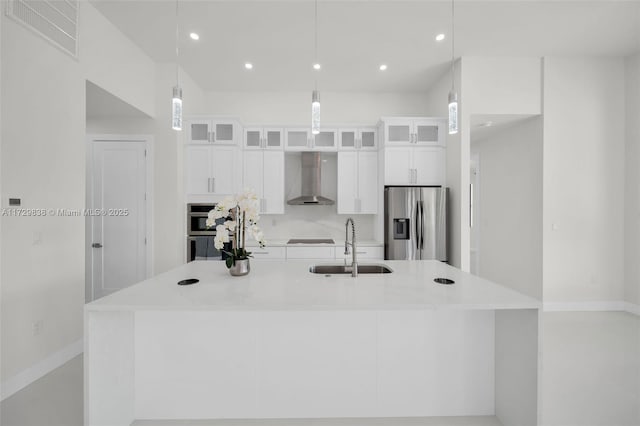 kitchen featuring wall chimney range hood, decorative light fixtures, white cabinets, sink, and stainless steel appliances