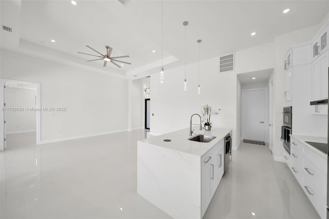 kitchen featuring white cabinetry, hanging light fixtures, a large island, sink, and a tray ceiling