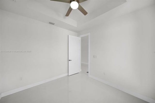 empty room featuring concrete flooring, a tray ceiling, and ceiling fan