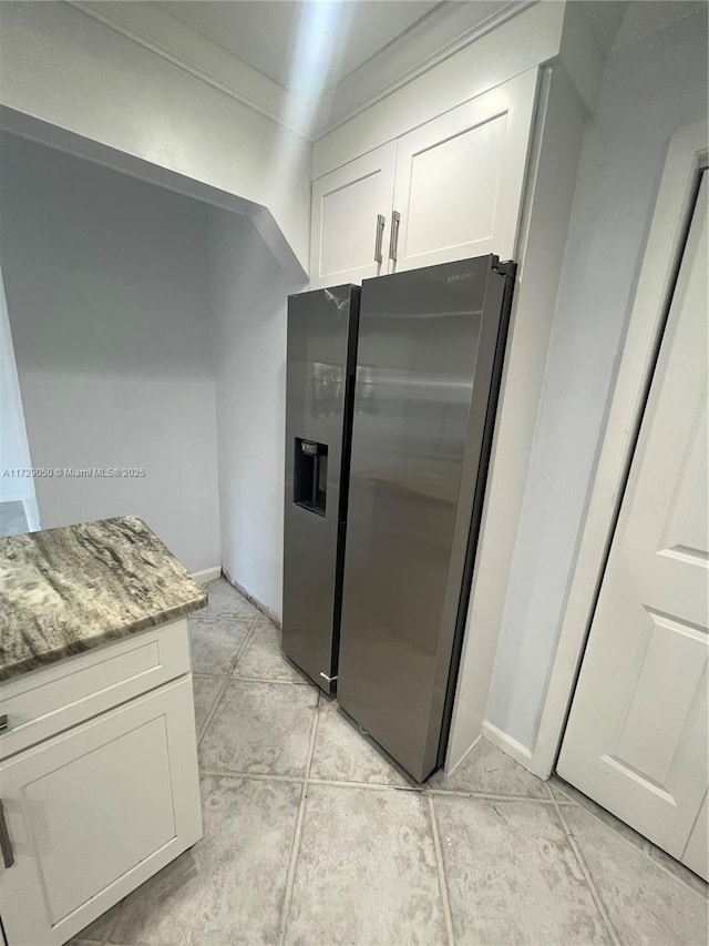 kitchen featuring white cabinets, light stone counters, light tile patterned floors, and stainless steel fridge