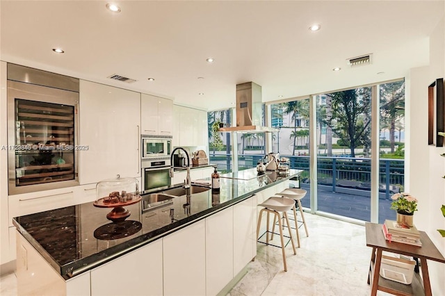 kitchen featuring beverage cooler, white cabinets, stainless steel appliances, dark stone counters, and floor to ceiling windows