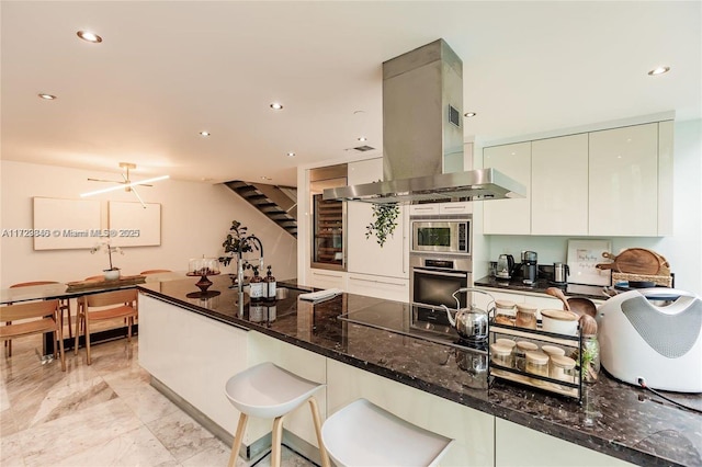 kitchen with kitchen peninsula, sink, island exhaust hood, dark stone countertops, and stainless steel appliances