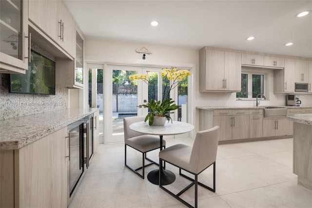 kitchen featuring light brown cabinetry, wine cooler, sink, light stone counters, and decorative backsplash