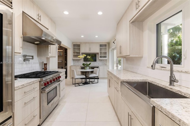 kitchen with appliances with stainless steel finishes, light brown cabinets, decorative backsplash, sink, and light stone counters