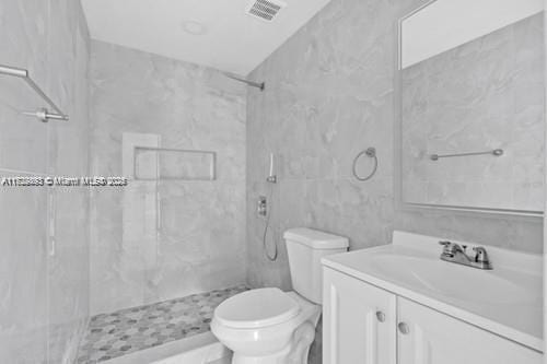 bathroom with toilet, vanity, and a tile shower