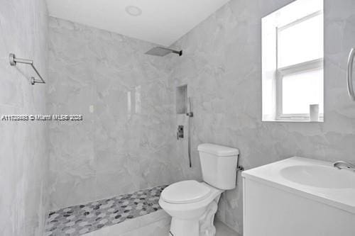 bathroom featuring a tile shower, toilet, and vanity