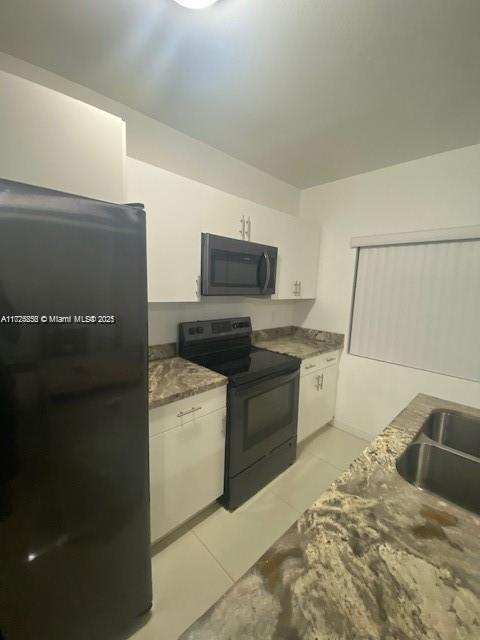 kitchen featuring black electric range, sink, white cabinets, light tile patterned flooring, and dark stone countertops